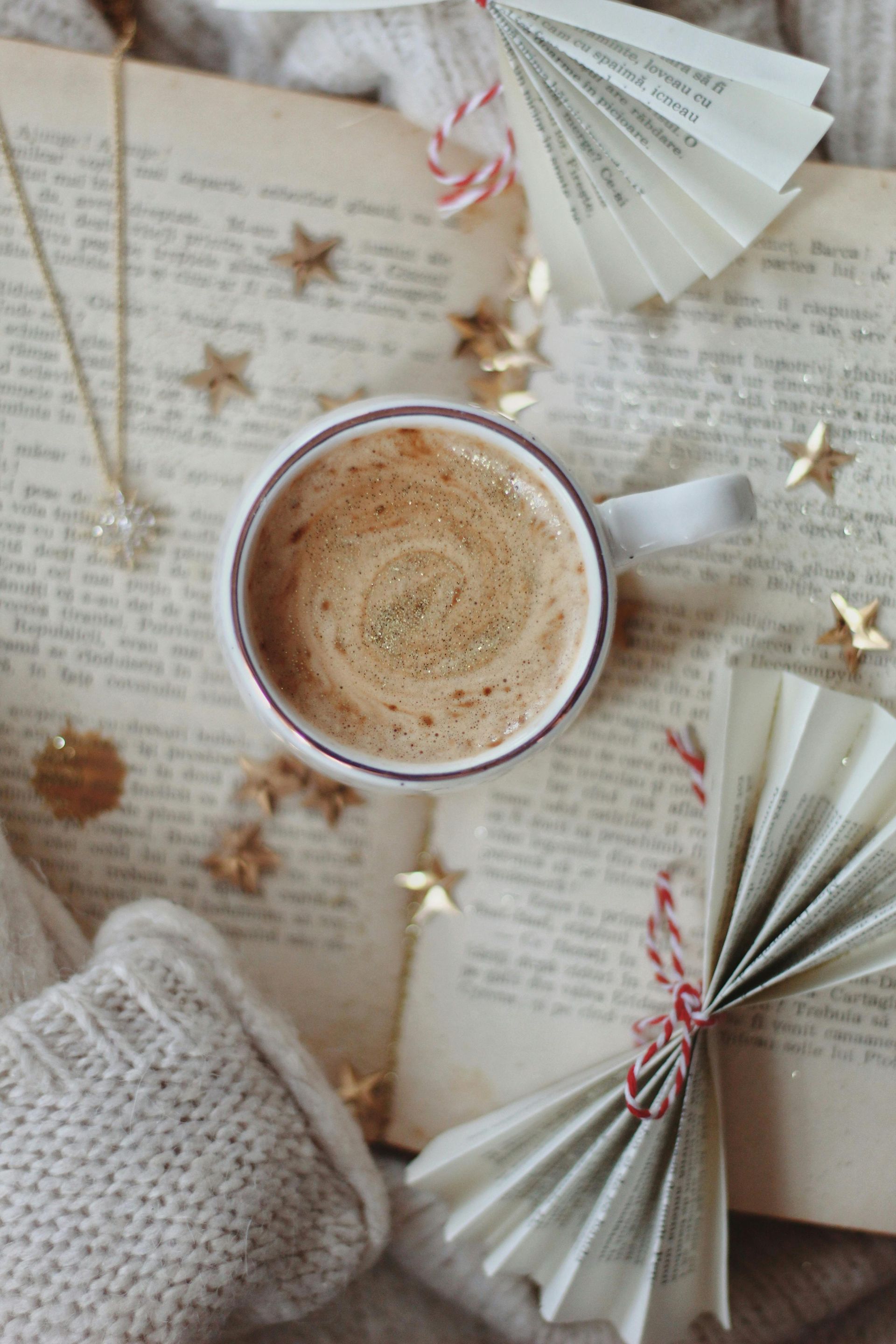 Coffee cup on open book, surrounded by stars and knitted sweater.