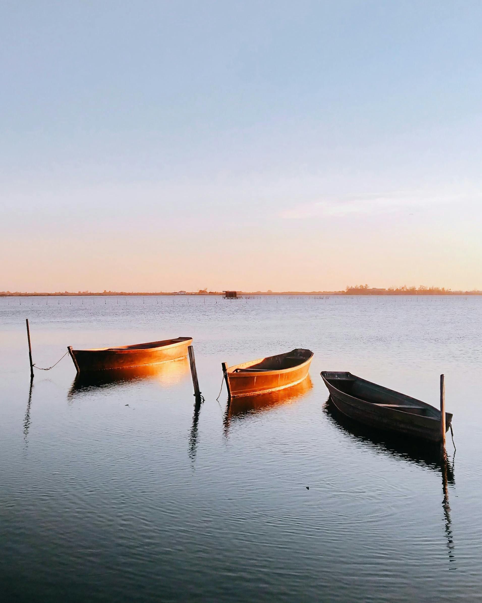 Three wooden boats floating in calm water with a sunset sky.