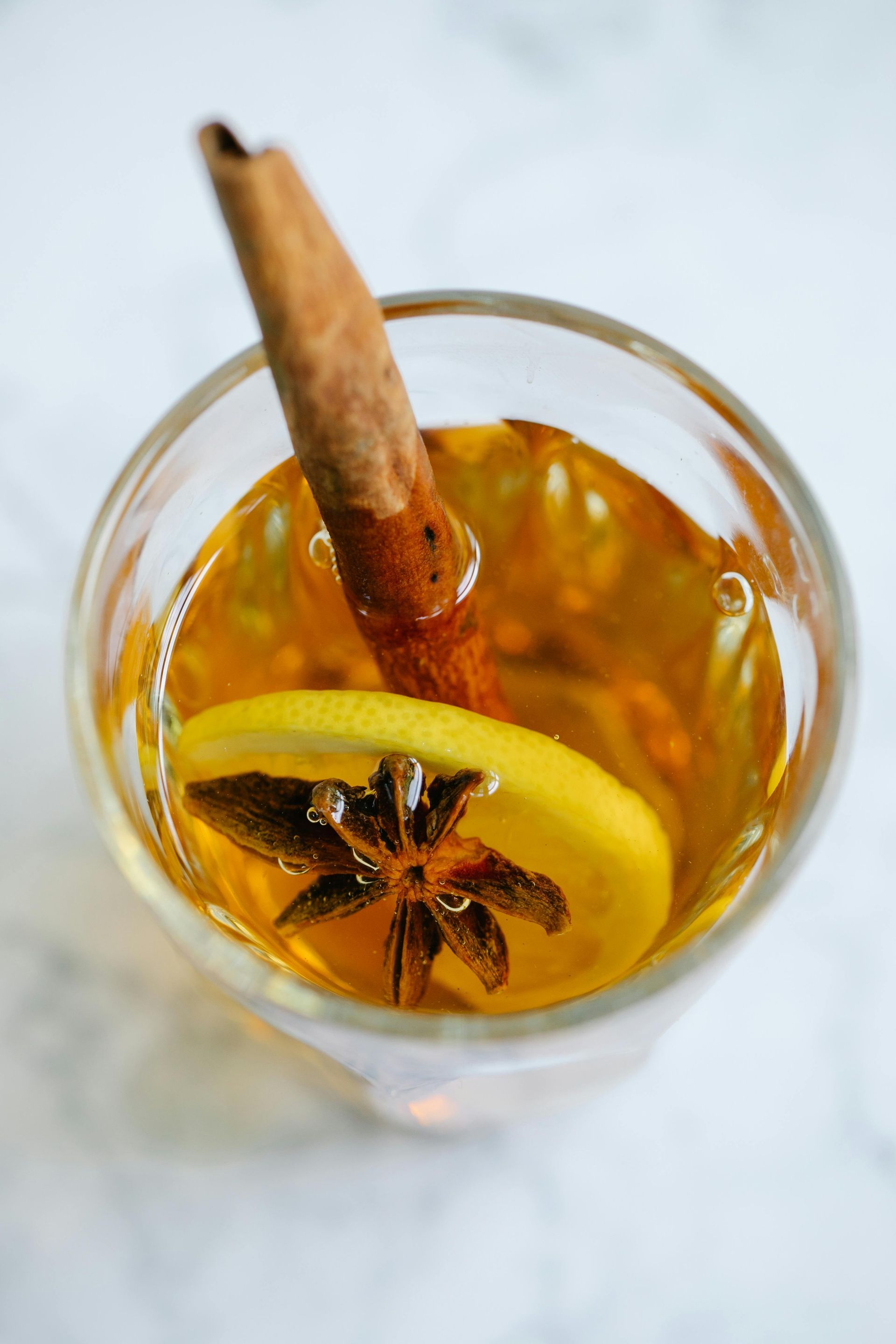 Glass of golden-colored drink with a cinnamon stick, lemon slice, and star anise.