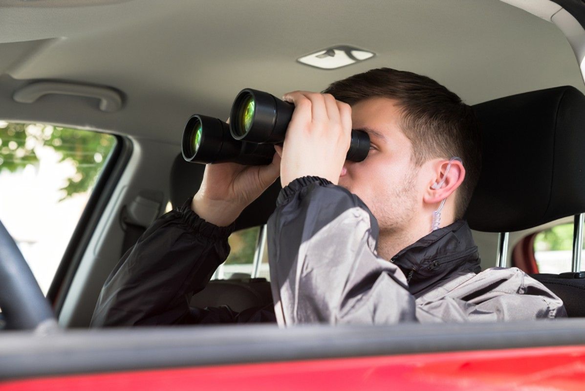 A man is sitting in a car looking through binoculars.