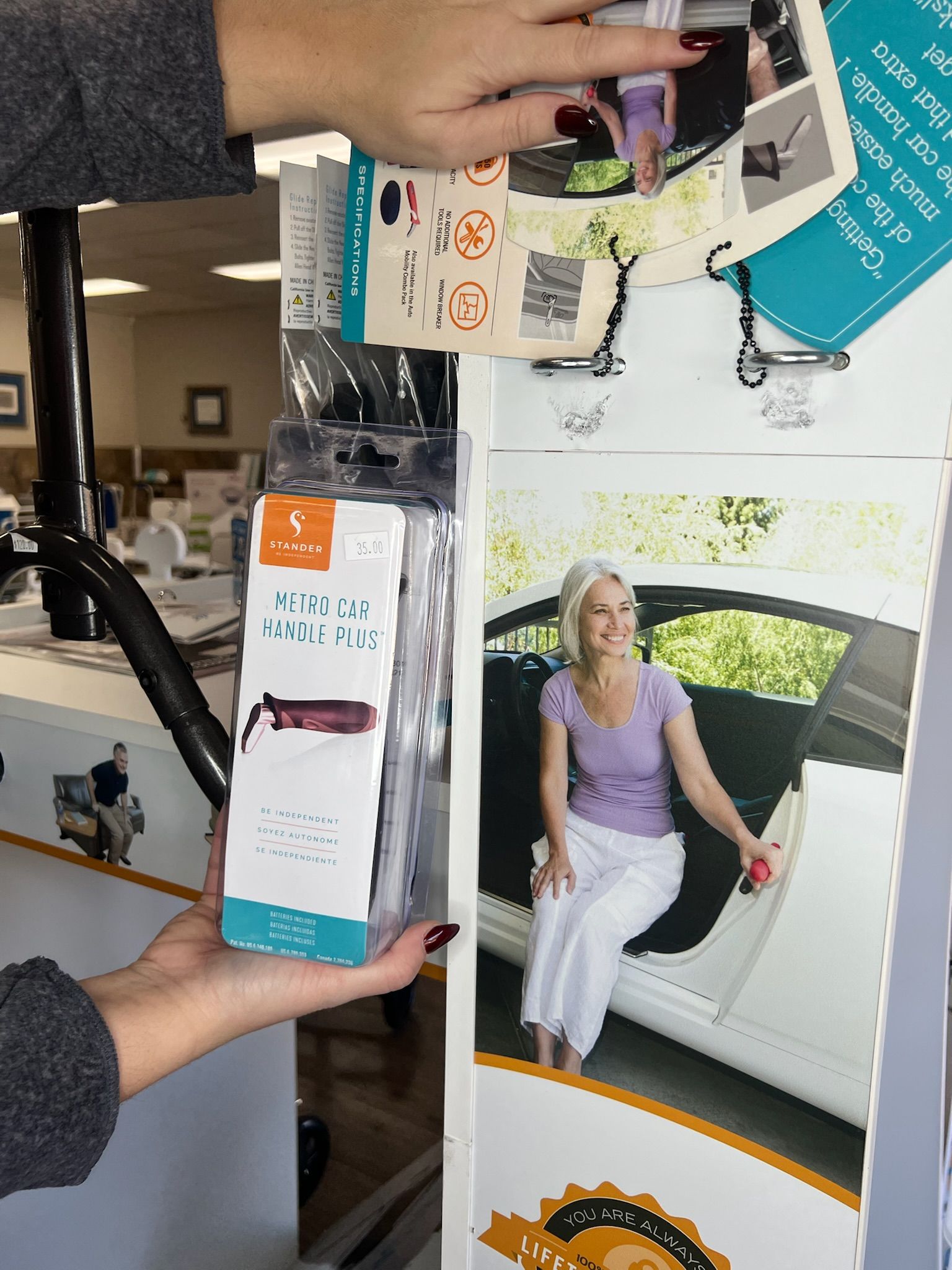 A person holds a product box for a car mobility handle next to a display showing someone using the device in a car.