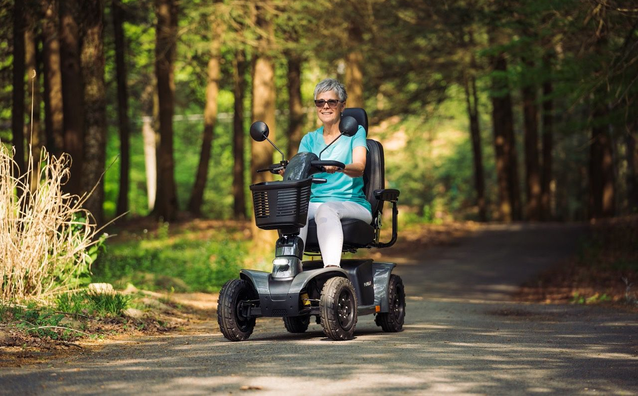 Woman riding a mobility scooter on a path in a wooded area.