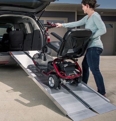 Woman loading a mobility scooter into a car using a ramp. The ramp is silver, the car is black.