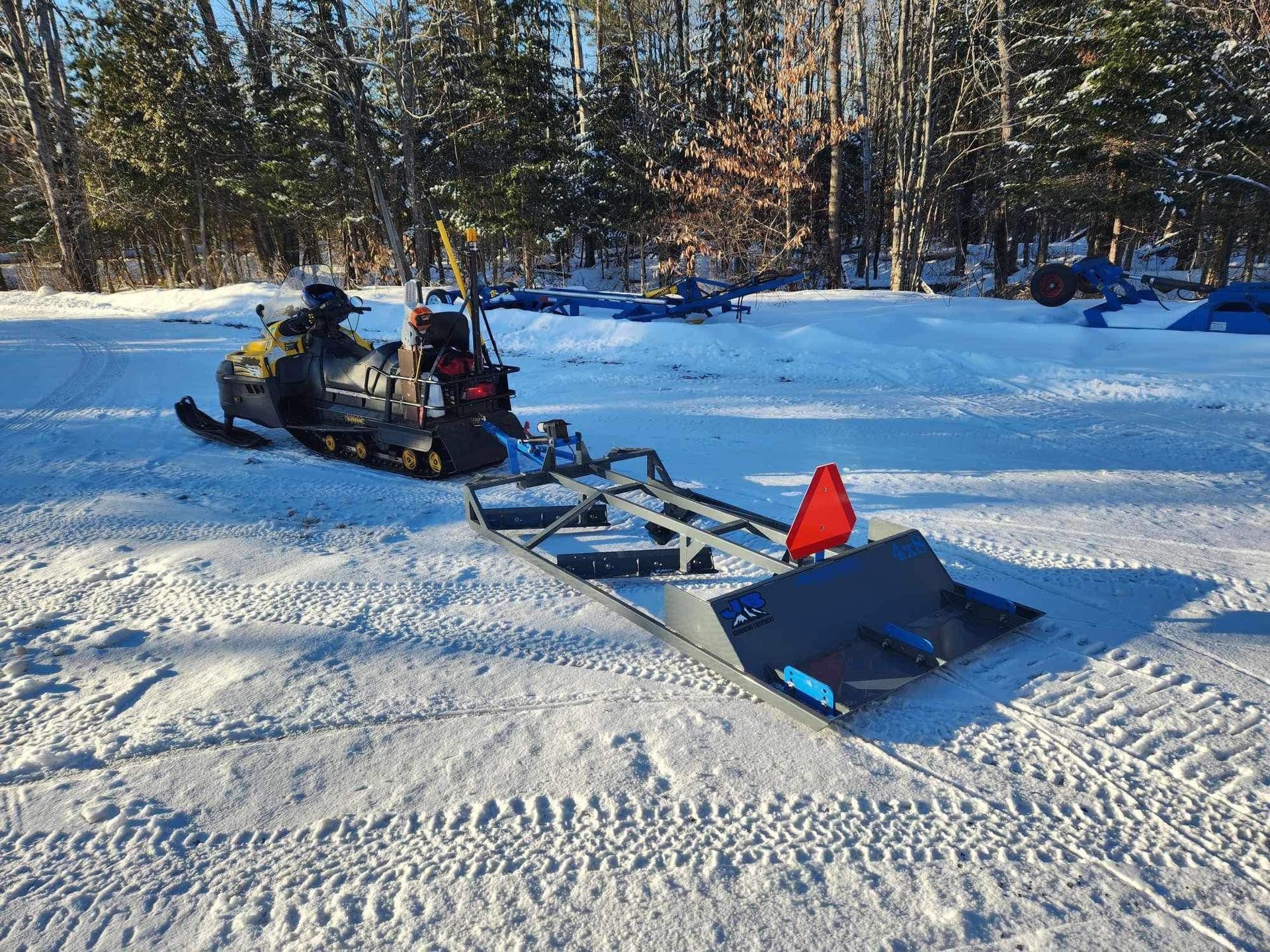 A snowmobile is parked in the snow with a plow attached to it.