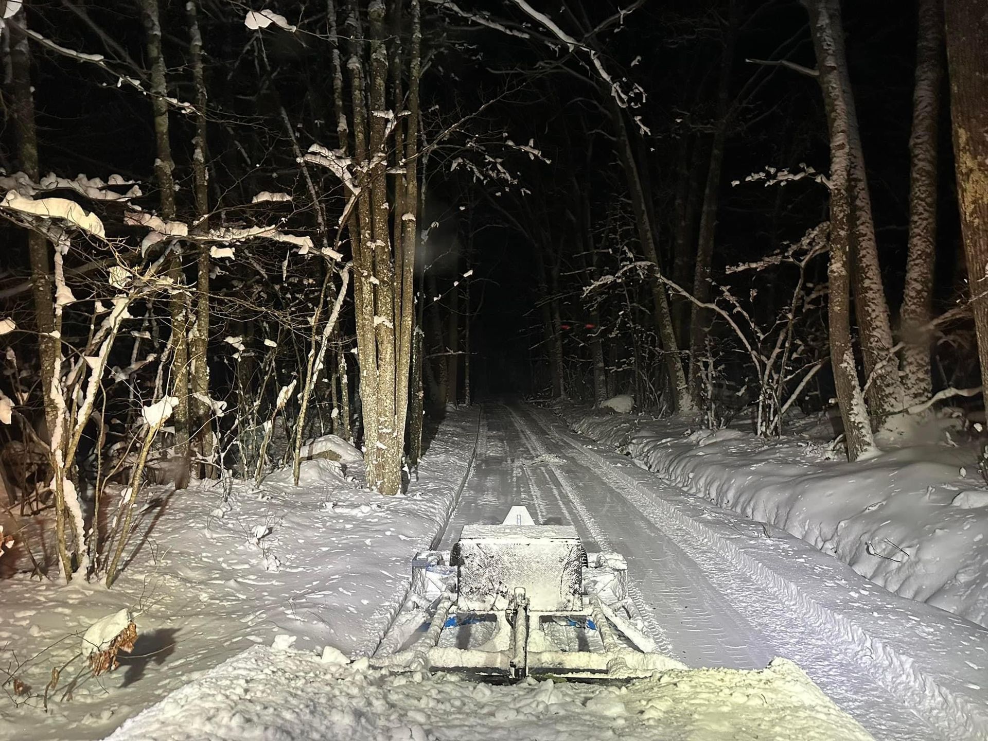 A snowmobile is driving down a snowy road at night.