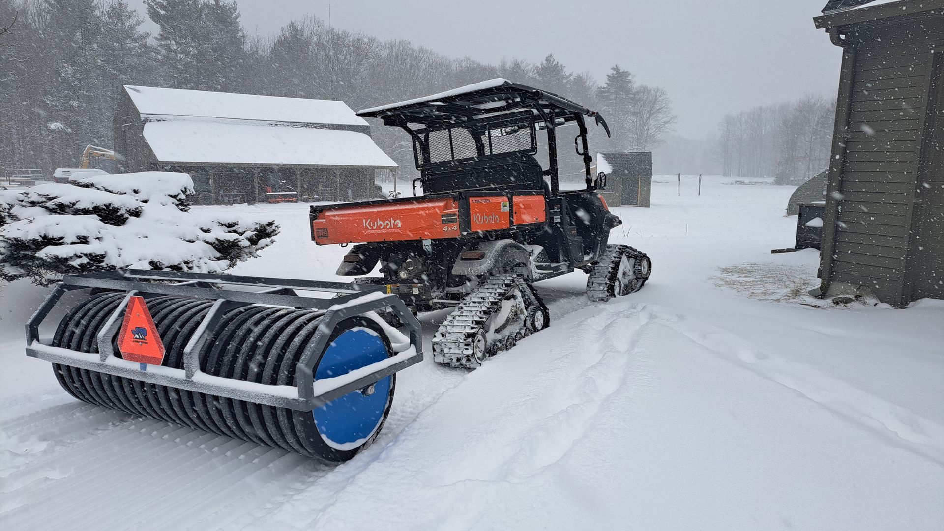 A tractor is parked in the snow with a roller attached to it.