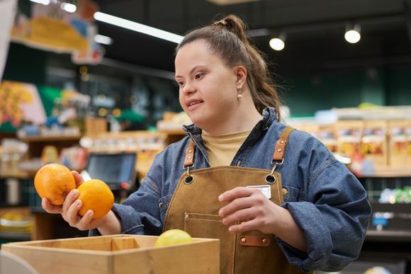 Shop worker placing oranges in a wooden crate at a grocery produce display