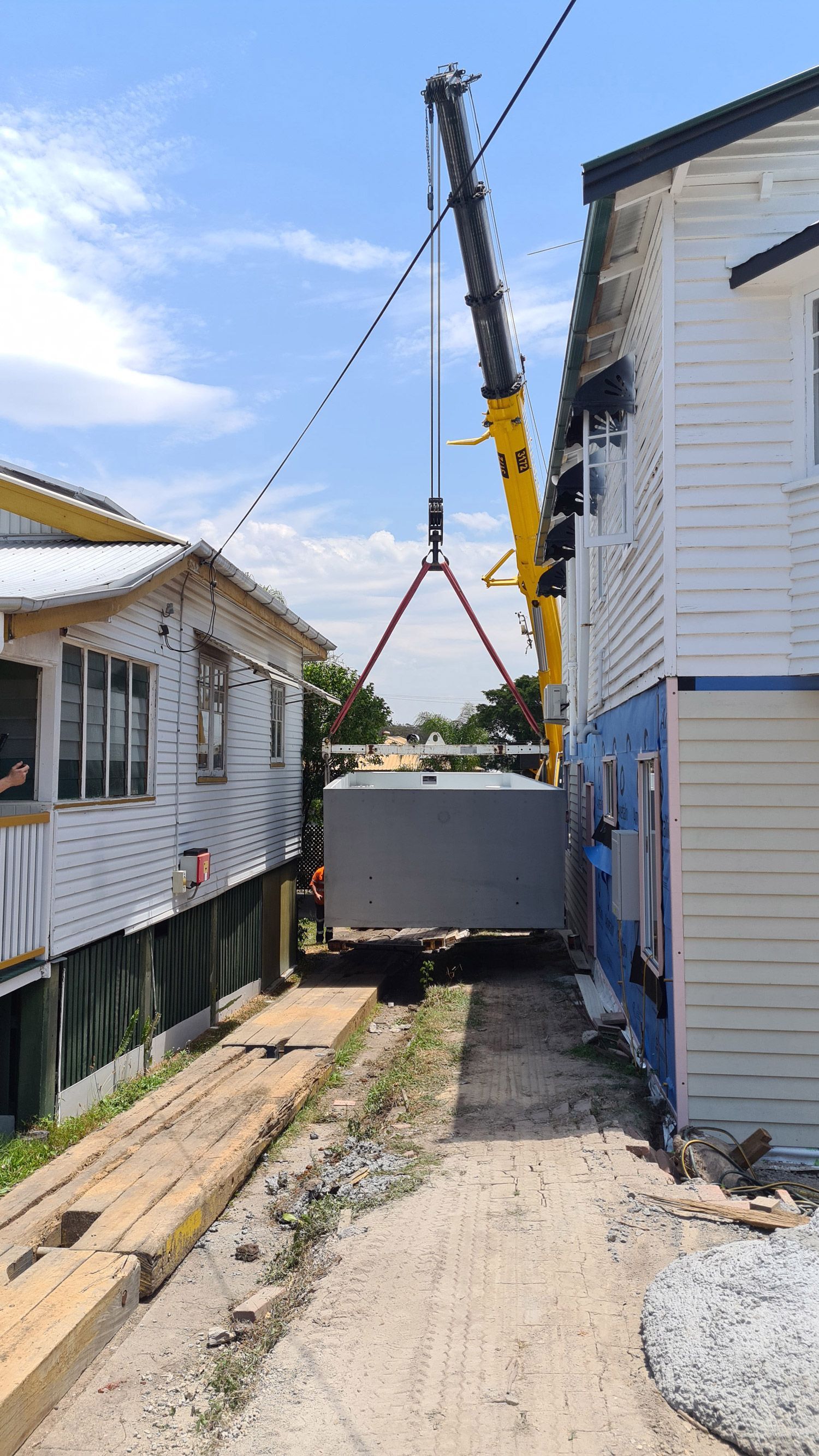 A crane is lifting a pre cast plunge pool between two buildings.