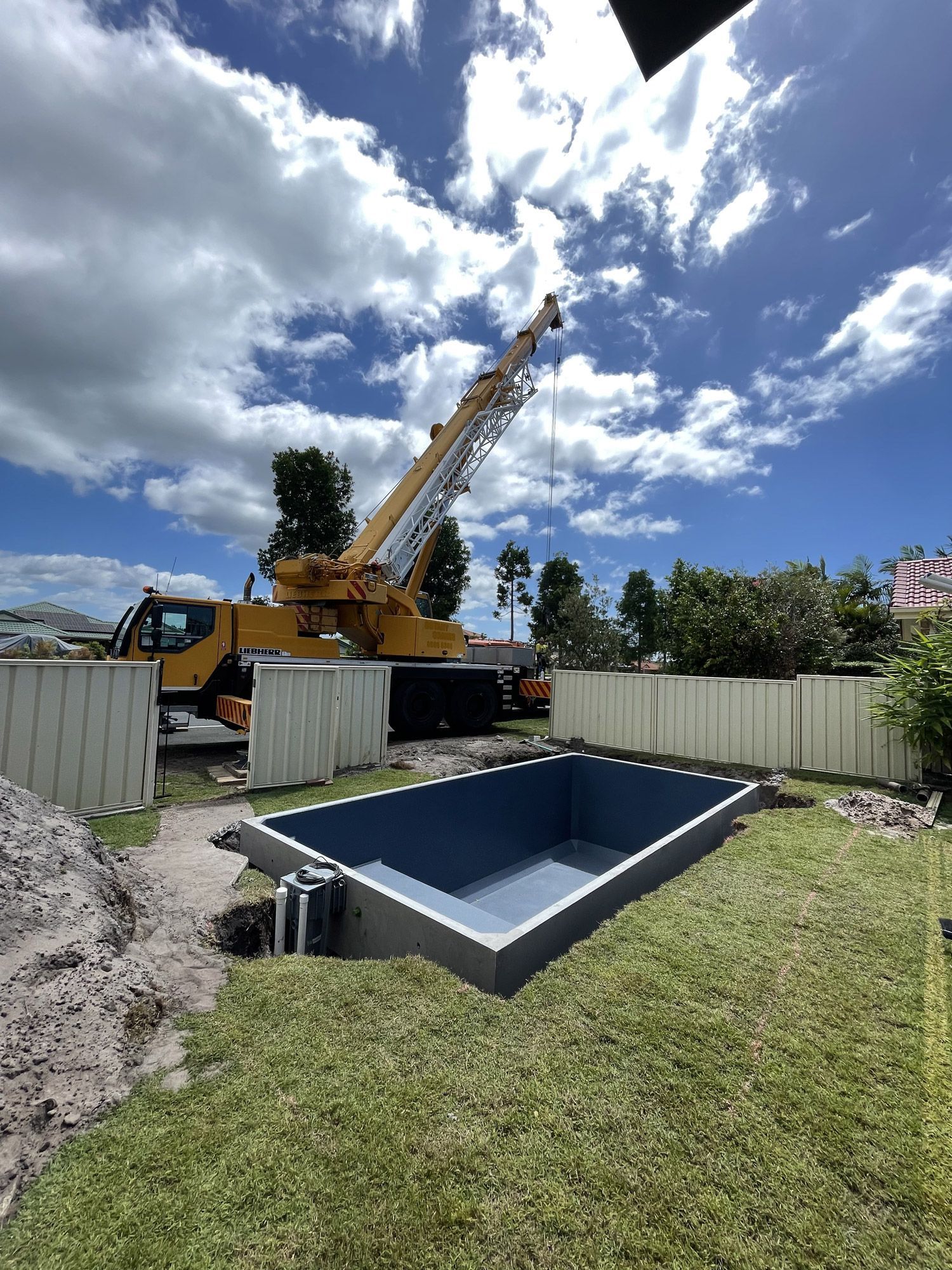 A crane is lifting a concrete plunge pool in a backyard.