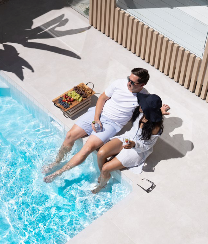 A man and a woman are sitting on the edge of a swimming pool.
