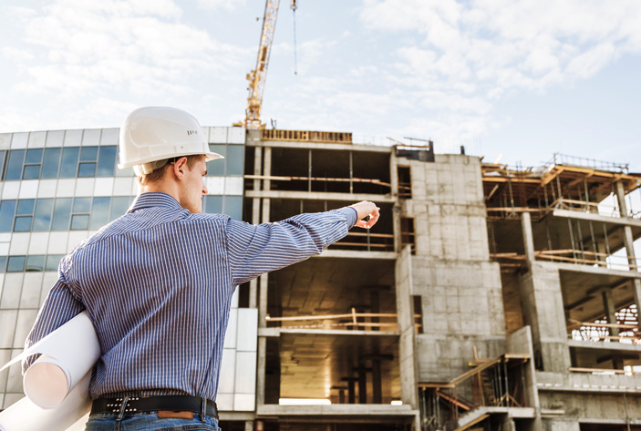 A man in a hard hat is pointing at a building under construction.
