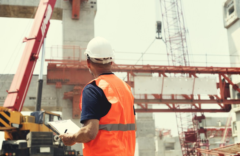 A construction worker is looking at a clipboard at a construction site.
