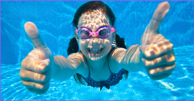 A little girl is swimming underwater and giving a thumbs up