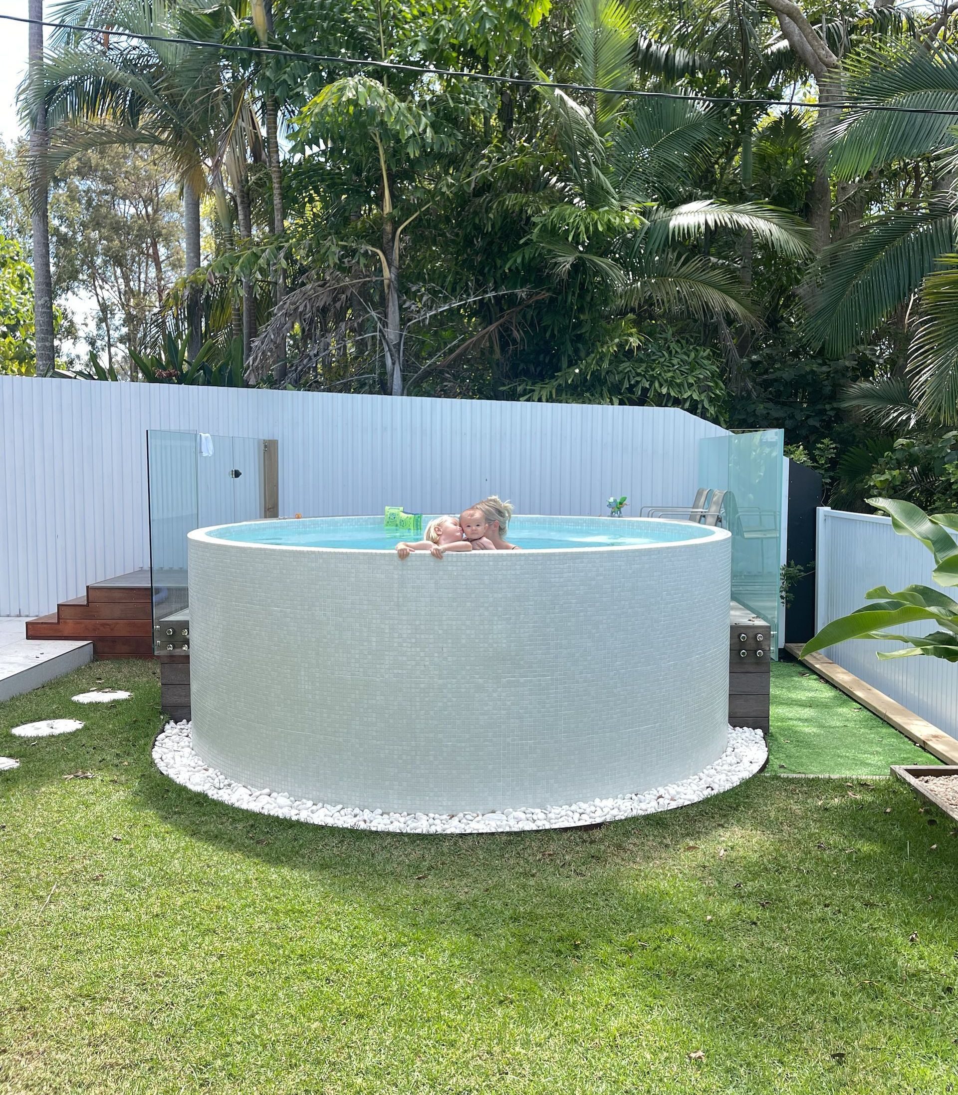 A family is swimming in a Plungie Arena above ground pool in a backyard. The exterior of the pool is fully tiled.