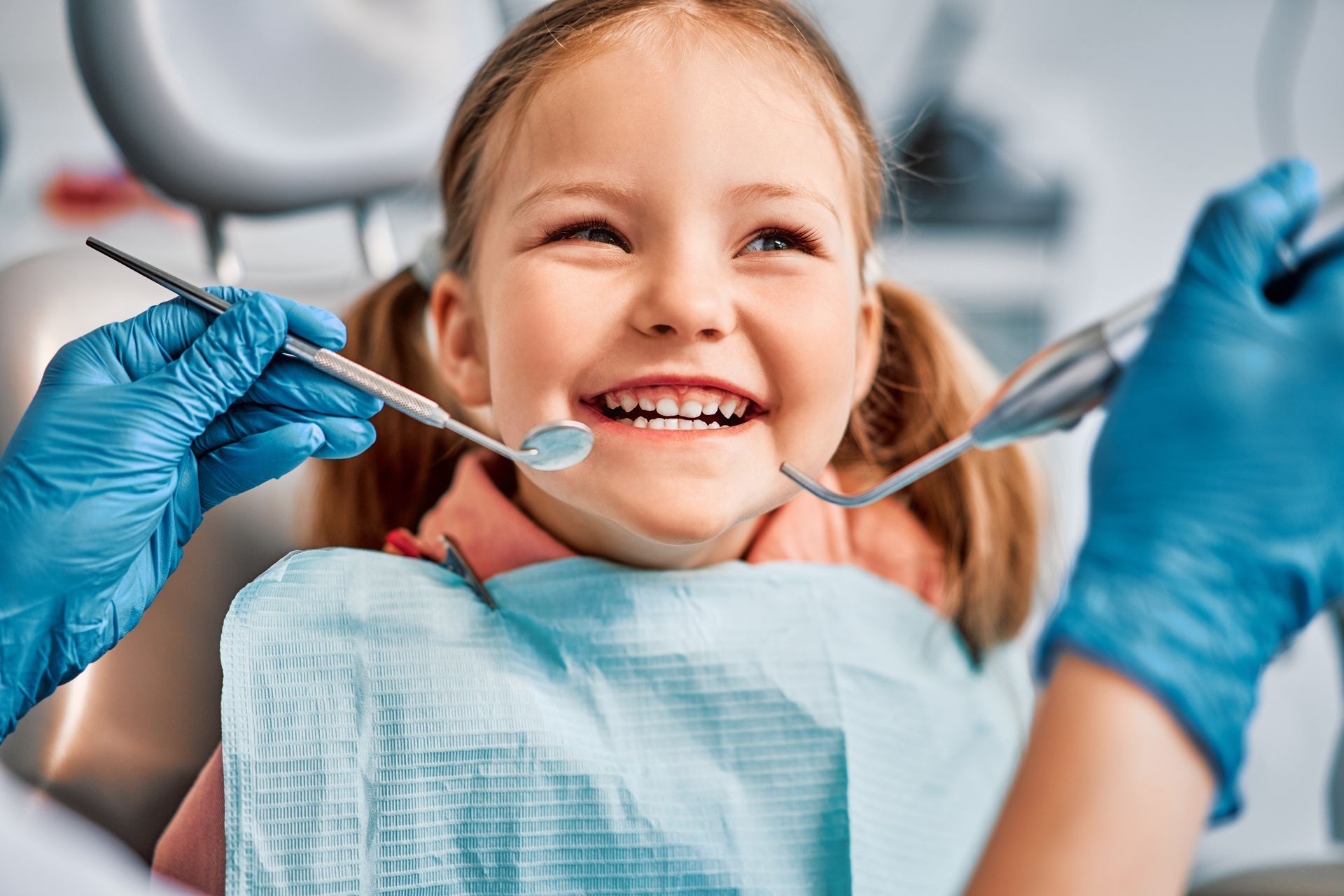 Gloved dental professional holding instruments while examining a patient.