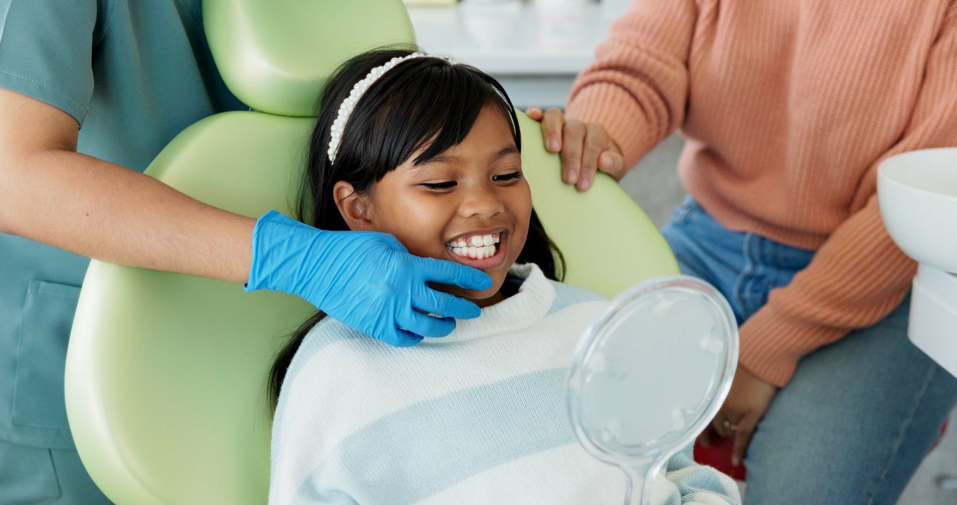 Dental professional supporting a child in a dental chair while a caregiver stands nearby.