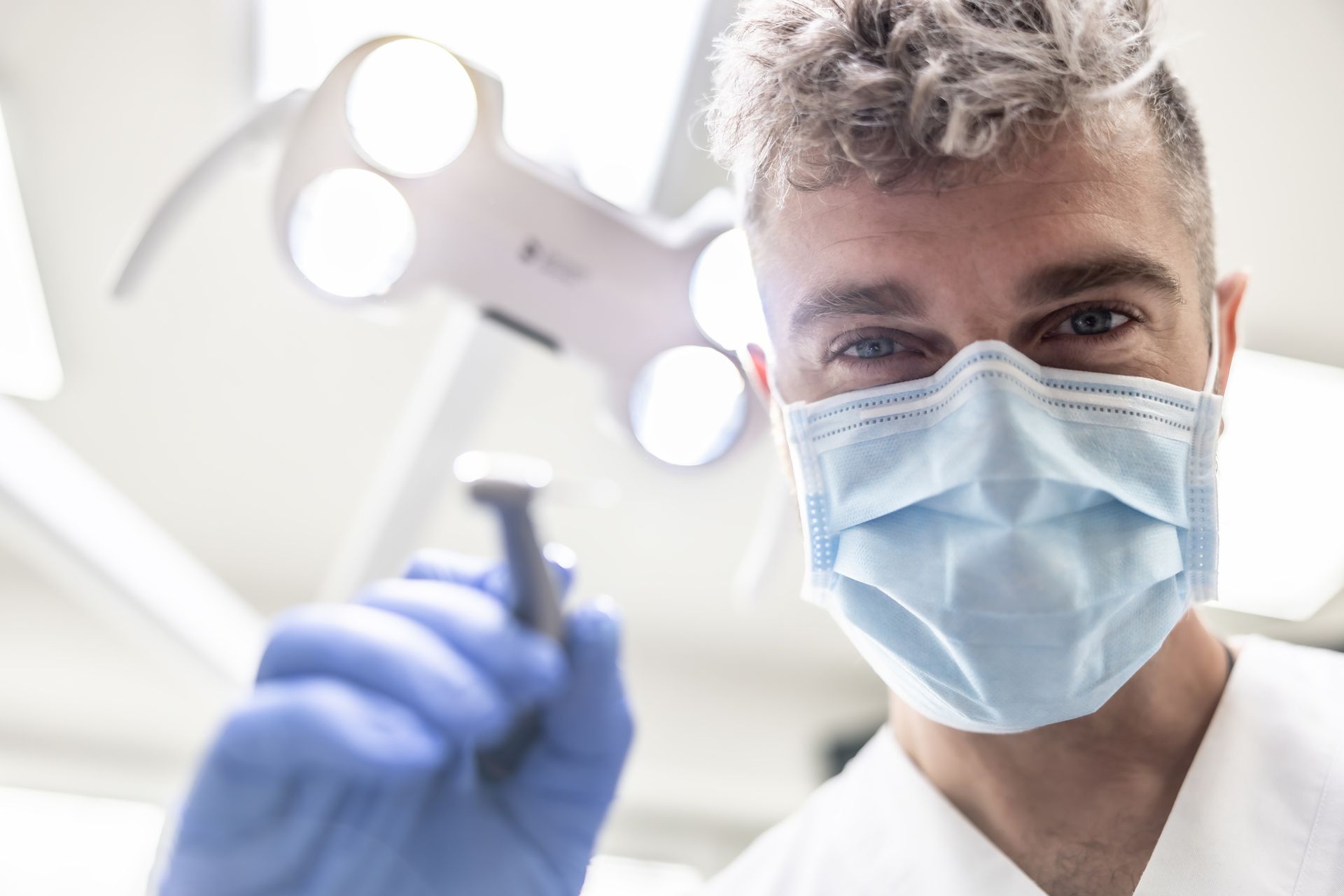 Below view of male dentist about to examine teeth with a tool at his office and looking at camera. Below view of male dentist about to examine teeth with a tool at his office and looking at camera.