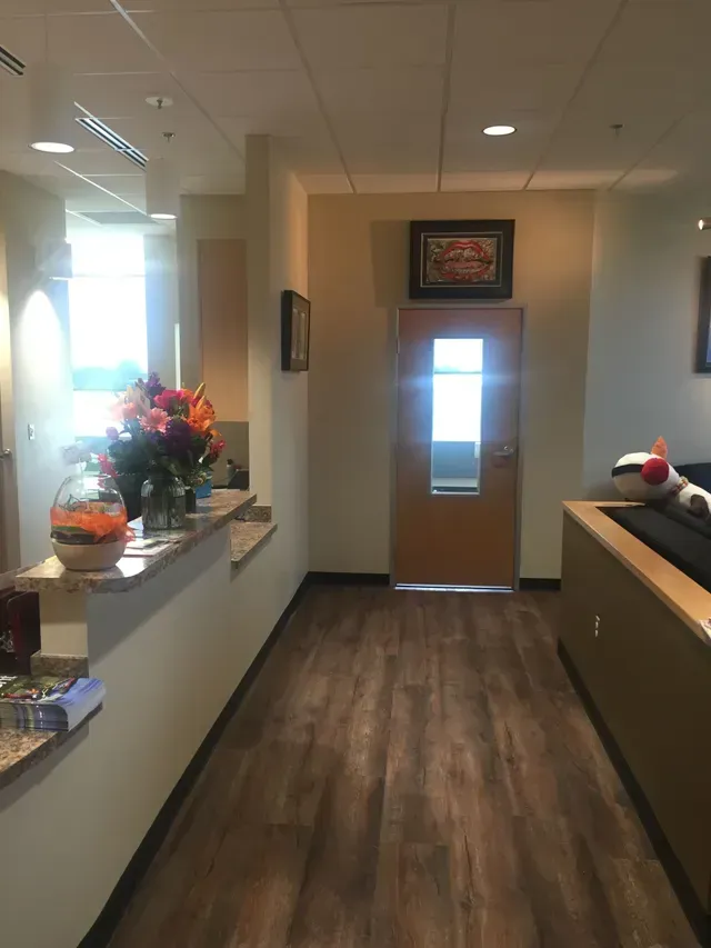 Hallway with wood-look floor, reception desk with flowers, and a door with window.