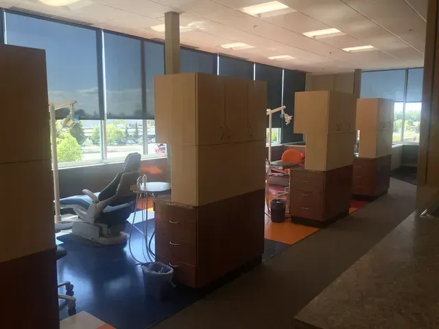 Dental office exam rooms with dark blue floors, tan cabinetry, and large windows.