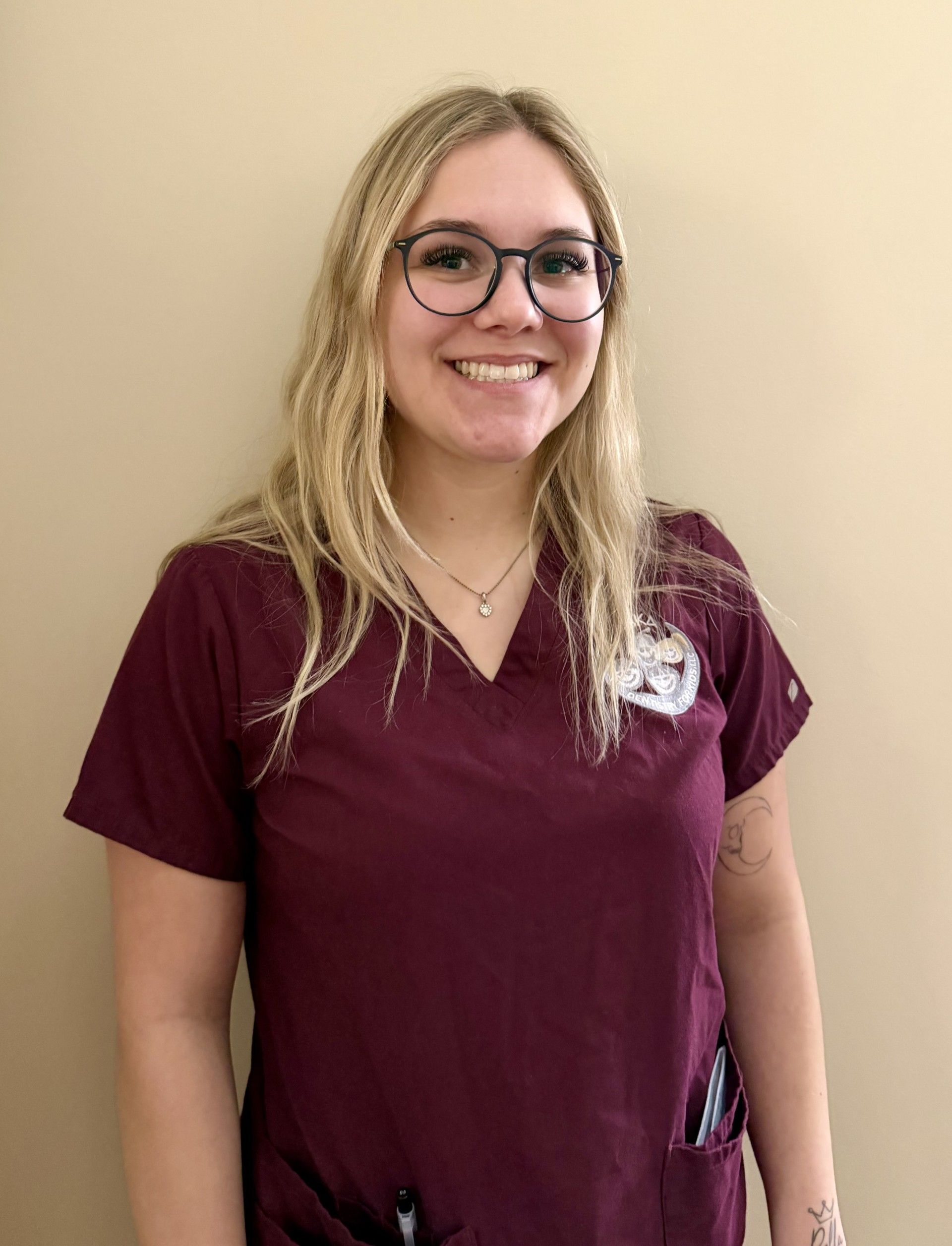Person with glasses smiling, wearing maroon scrubs with 