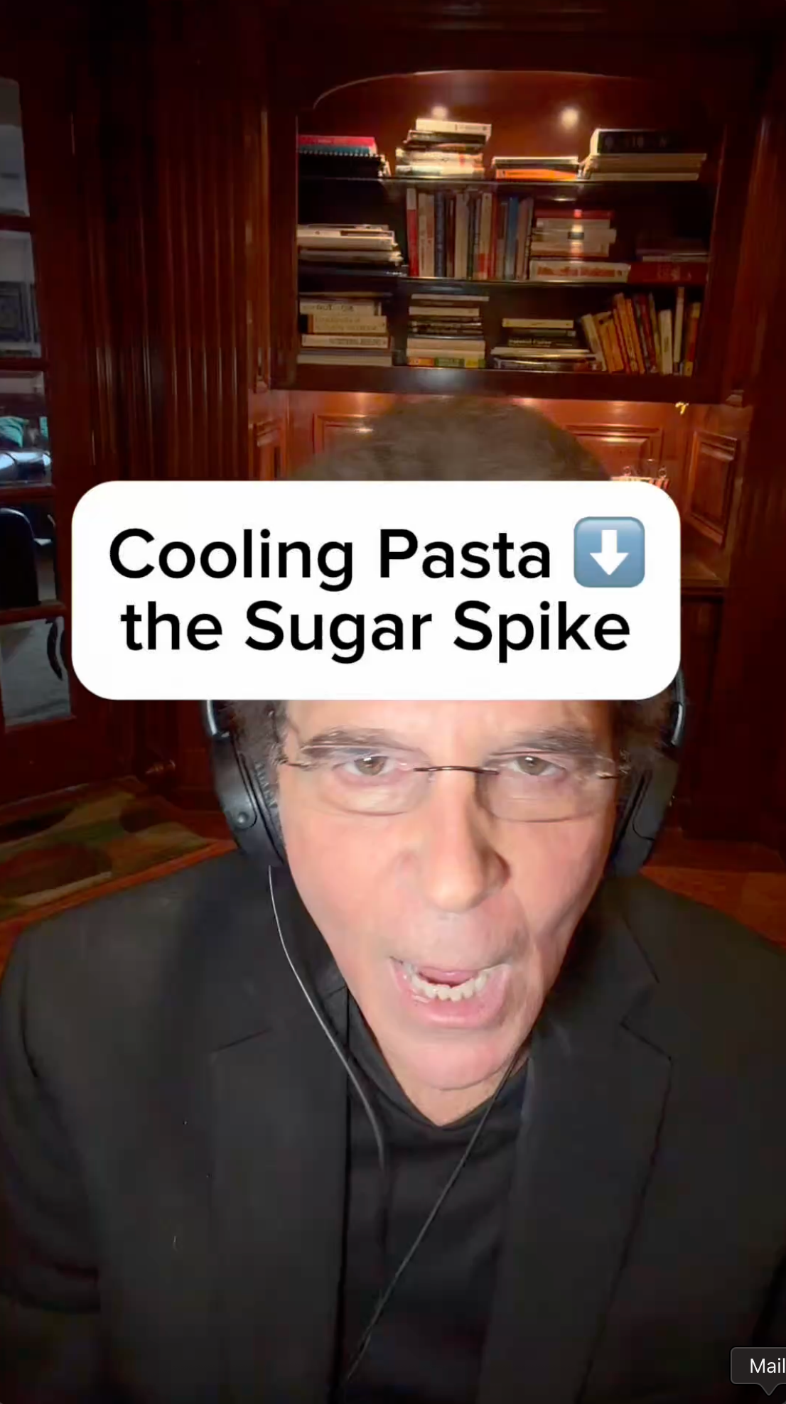 Man in black suit with headset, speaking. Text: Cooling Pasta, the Sugar Spike. Bookshelf background.