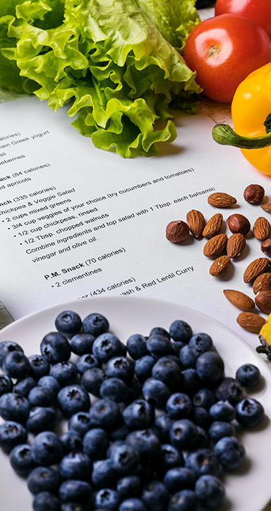 A plate of blueberries , almonds , tomatoes , lettuce and other vegetables on a table.