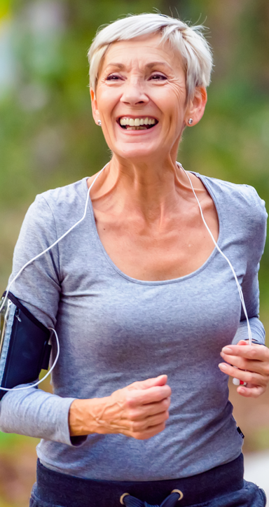 An older woman is smiling while running and listening to music.