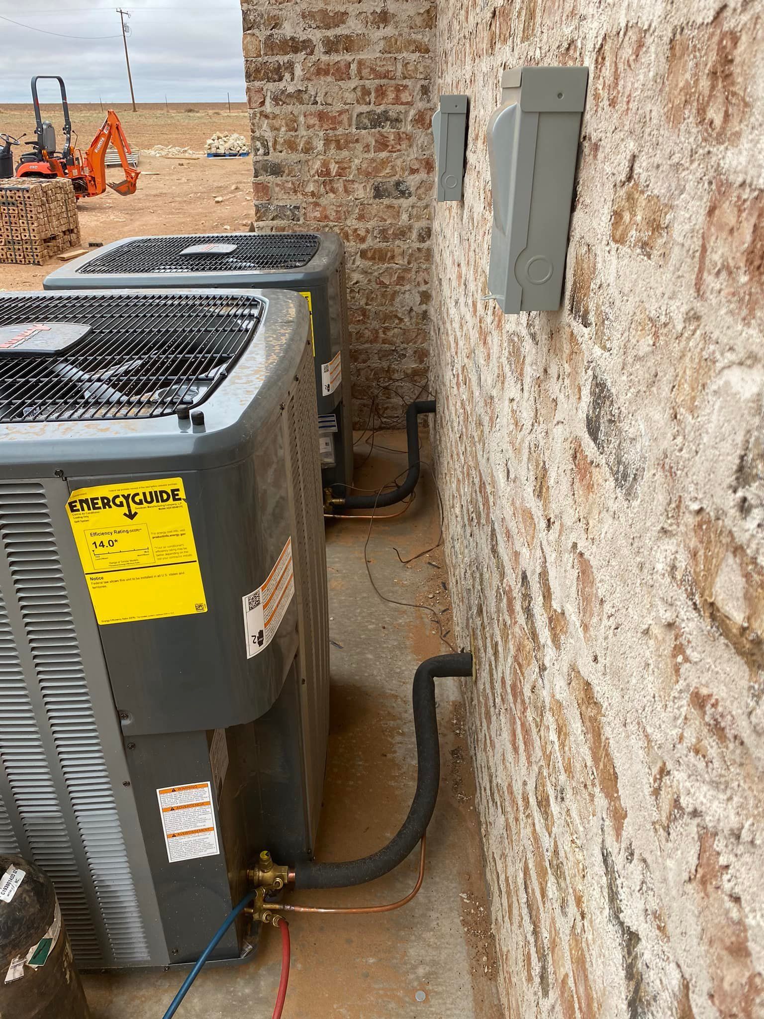 Two AC units next to a brick wall with electrical boxes, construction site in the background.