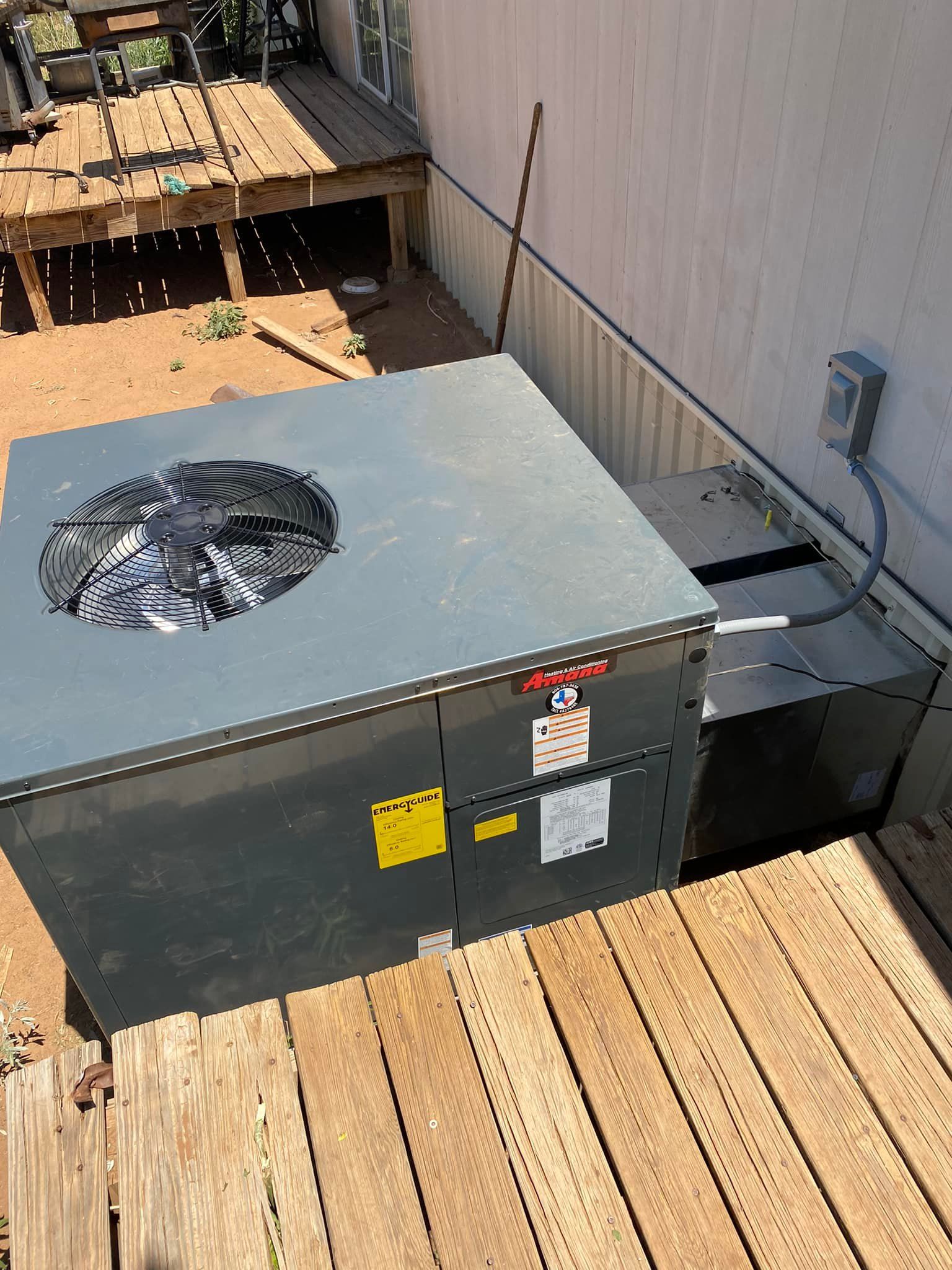 Gray HVAC unit on wooden deck next to a wall with electrical box.