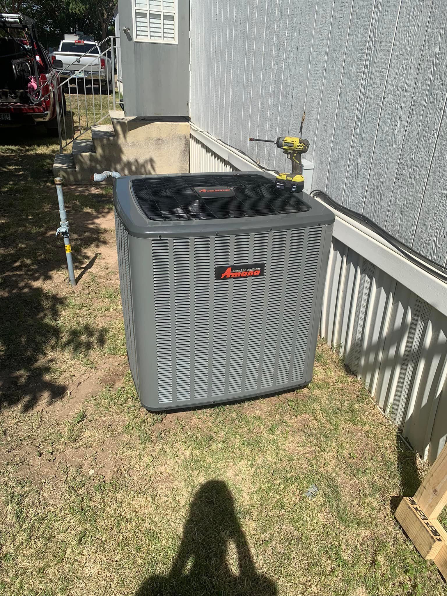 Outdoor air conditioner unit next to a building, in a yard with dry grass.
