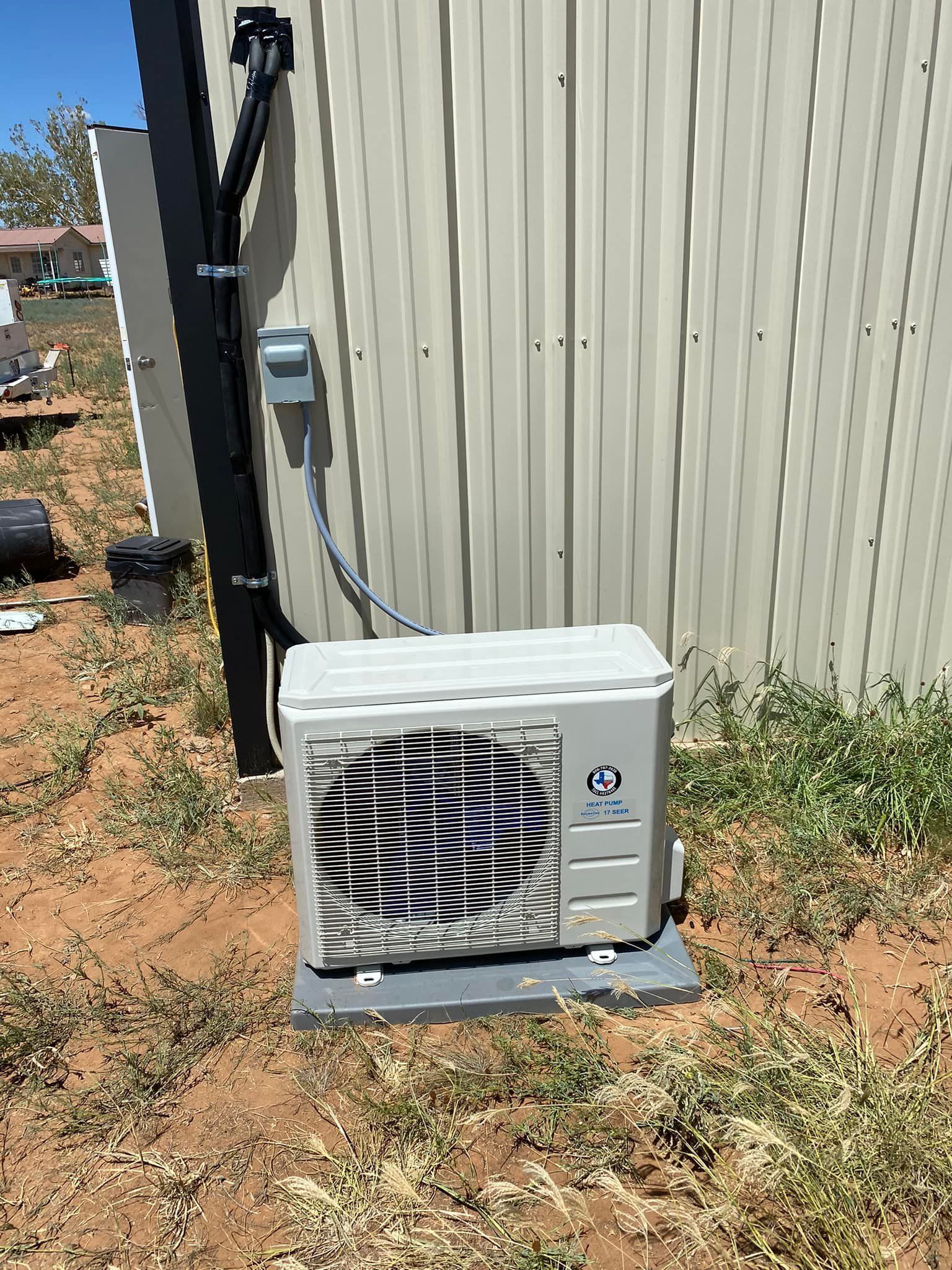 Air conditioner unit on a concrete pad outside a metal building. Electrical conduit and box are visible.