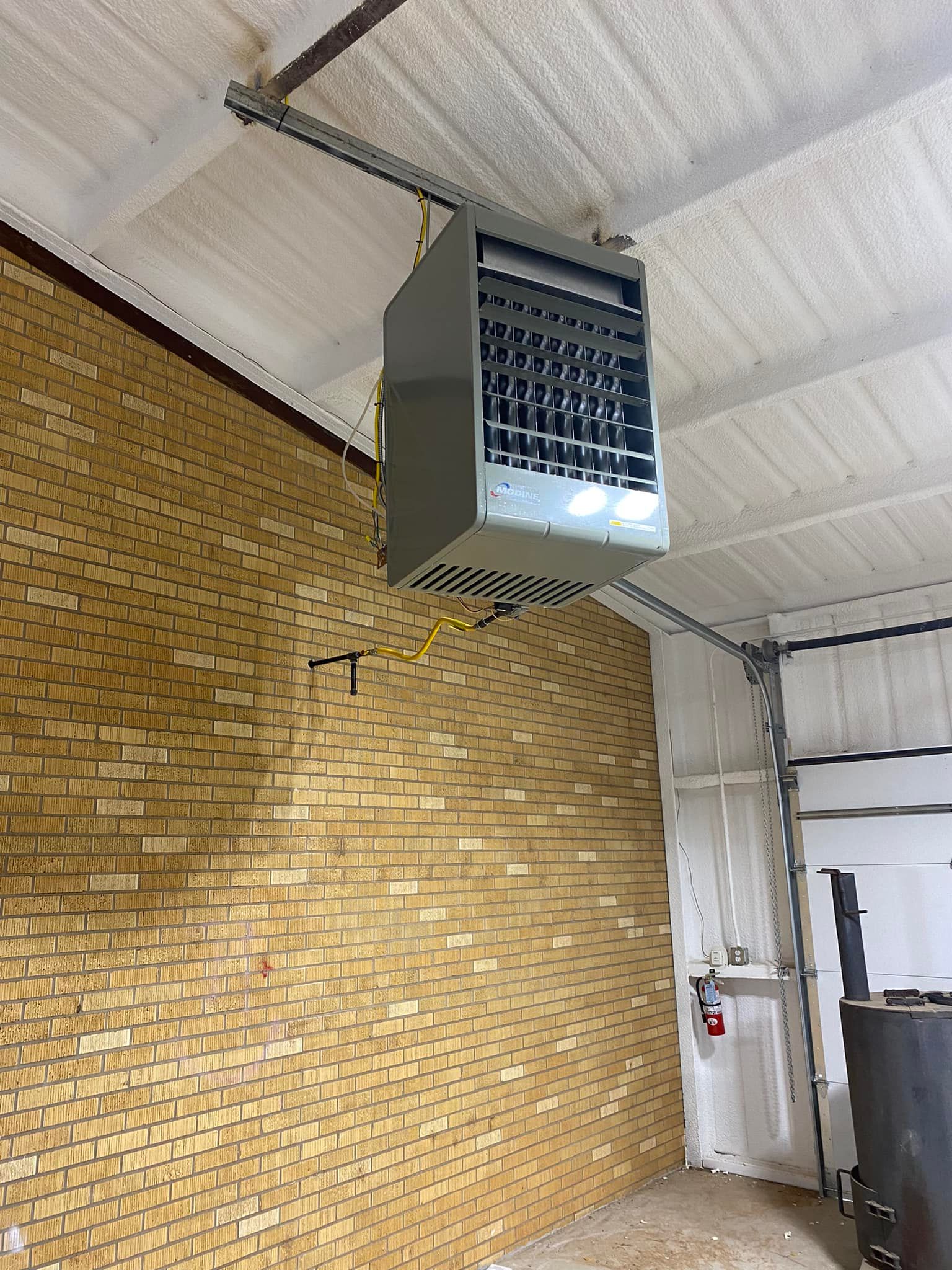Gray ceiling-mounted industrial heater in a brick-walled workshop.