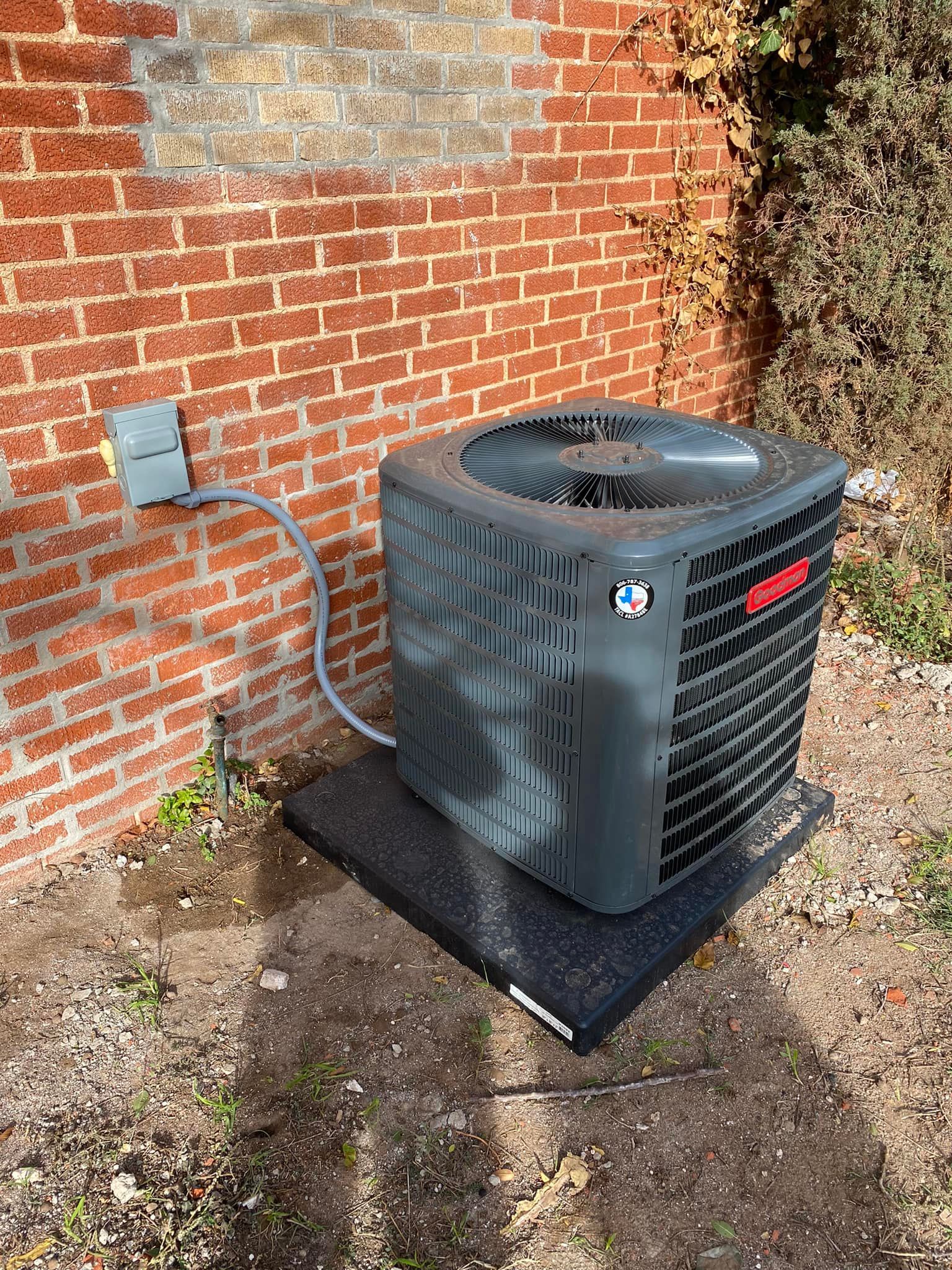Outdoor air conditioning unit against a red brick wall.