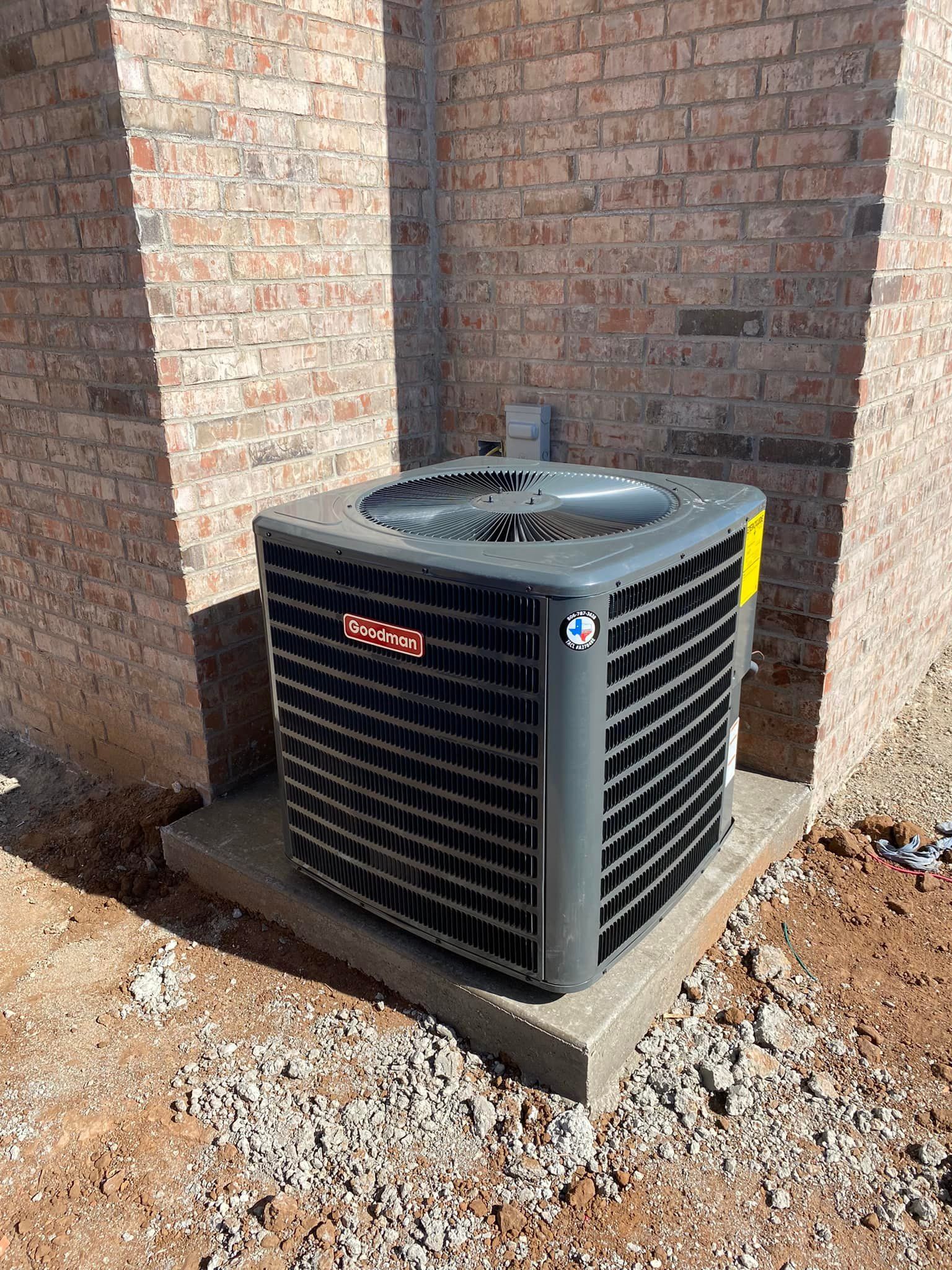 Air conditioning unit set on a concrete pad, next to a brick wall.