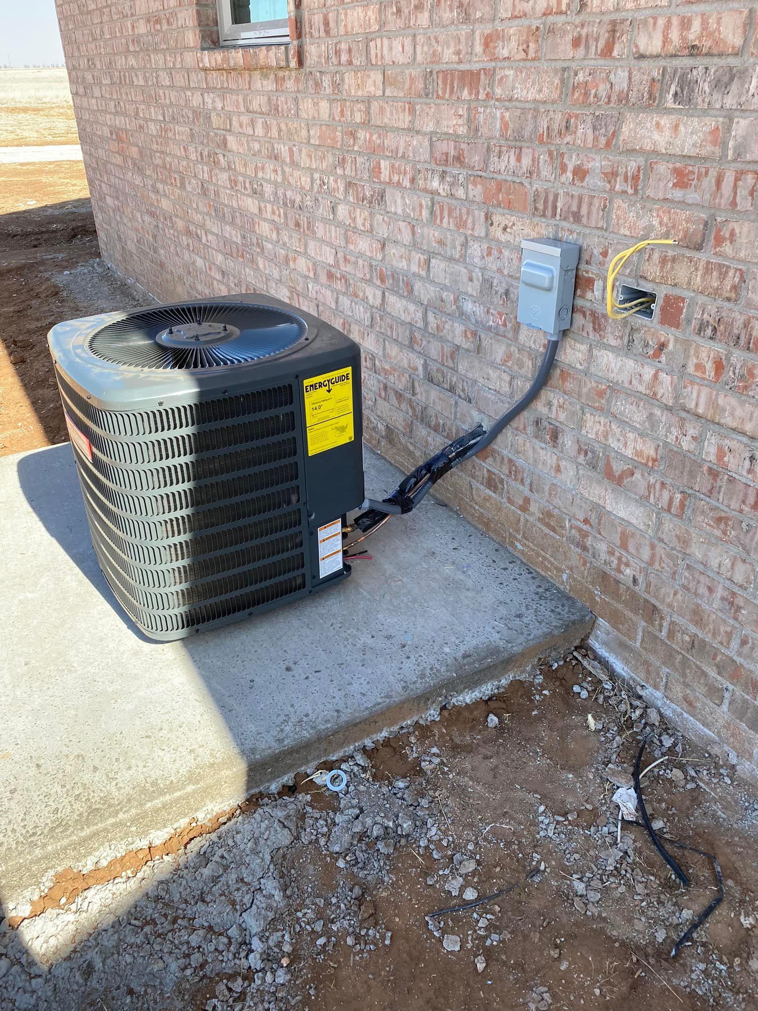 Air conditioning unit on a concrete pad near a brick wall with electrical wiring.