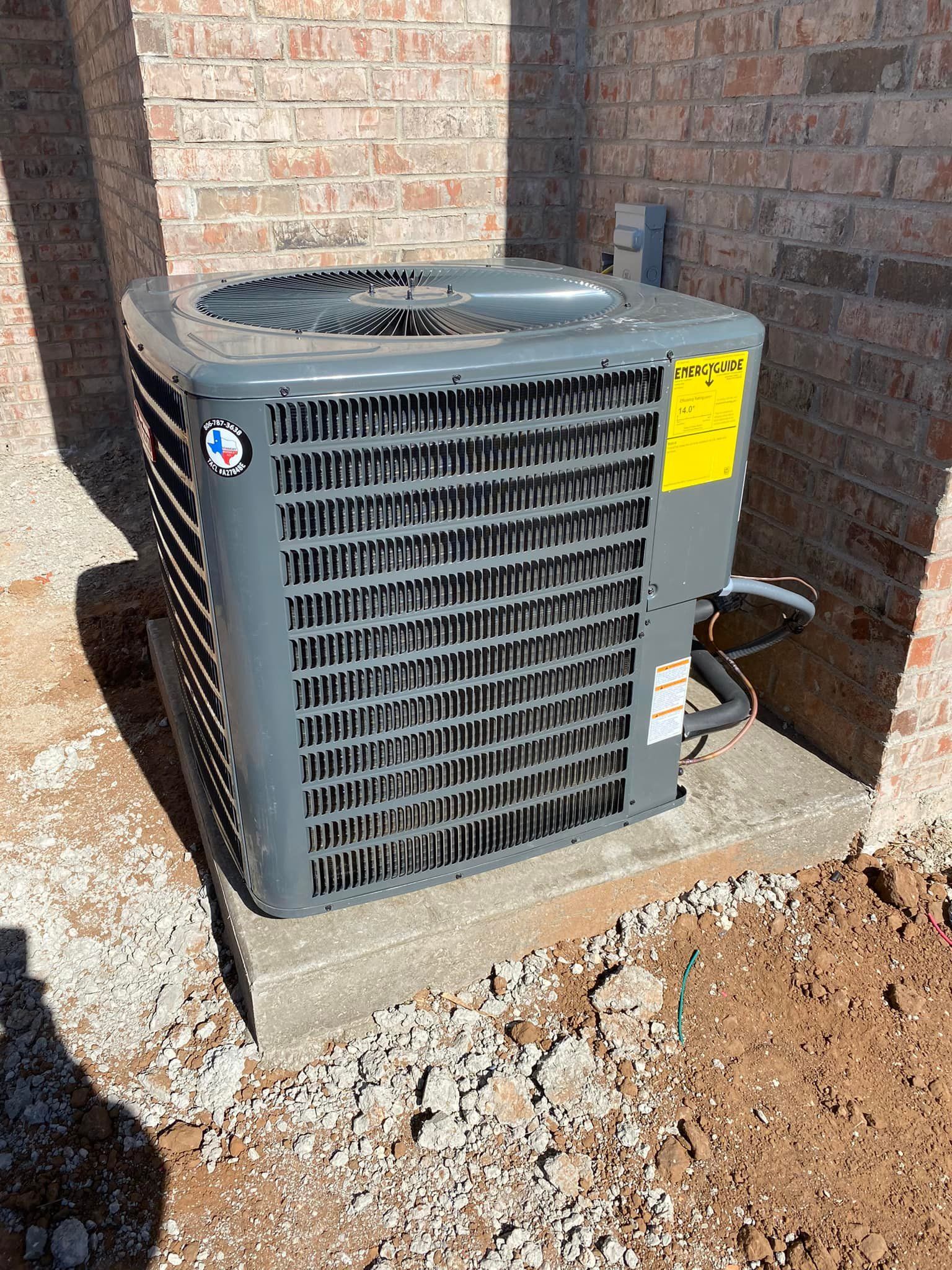 Gray air conditioning unit on a concrete pad next to a brick wall.