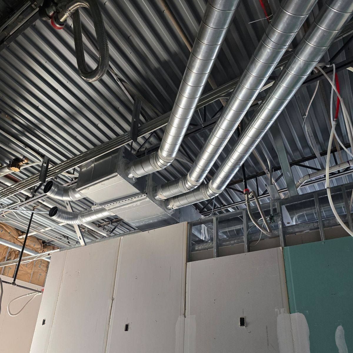 HVAC ductwork and electrical wiring installed on a corrugated metal ceiling in a construction setting.