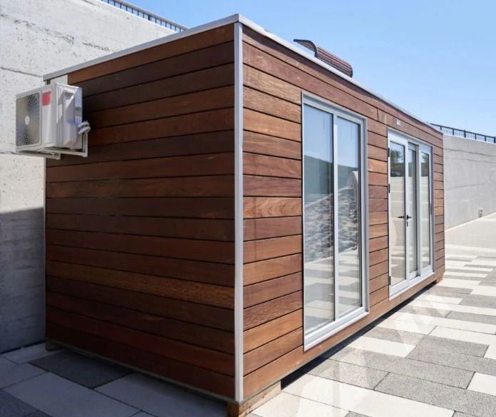 Wooden cabin with large windows and air conditioning unit, on a tiled surface.