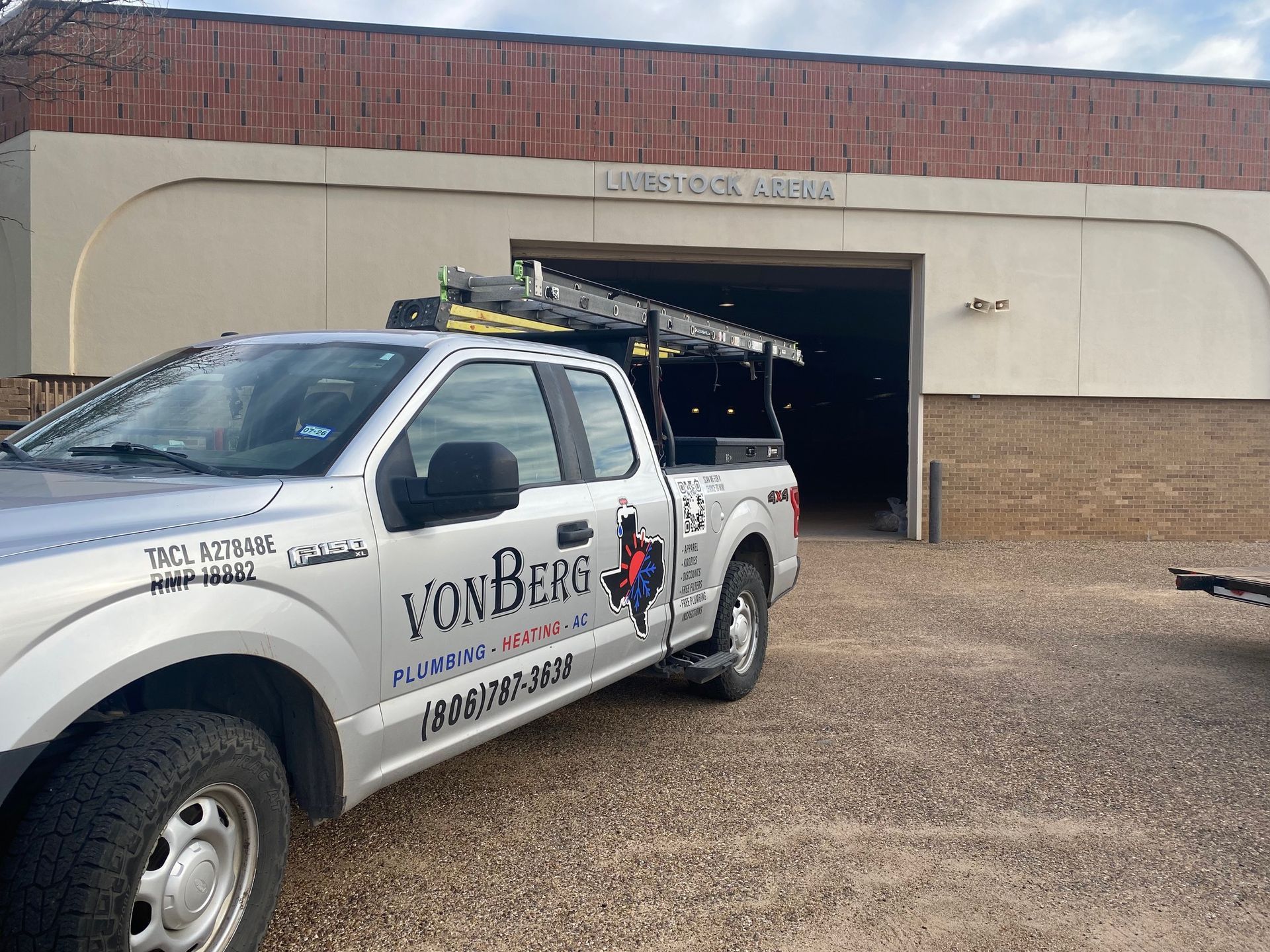 Silver VonBerg service truck parked in front of a building with an open bay door.