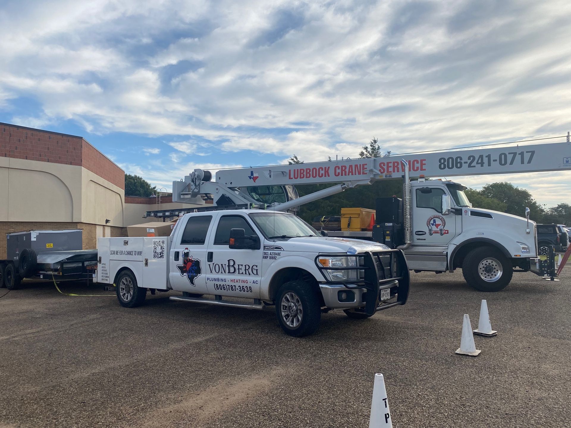 Two white work trucks with cranes parked in a lot, one with the Texas flag logo.