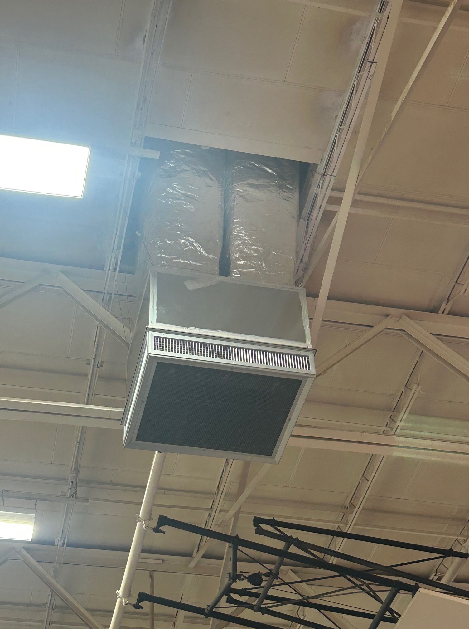 Ceiling-mounted HVAC unit with metal frame and visible ductwork in a building with steel support beams.