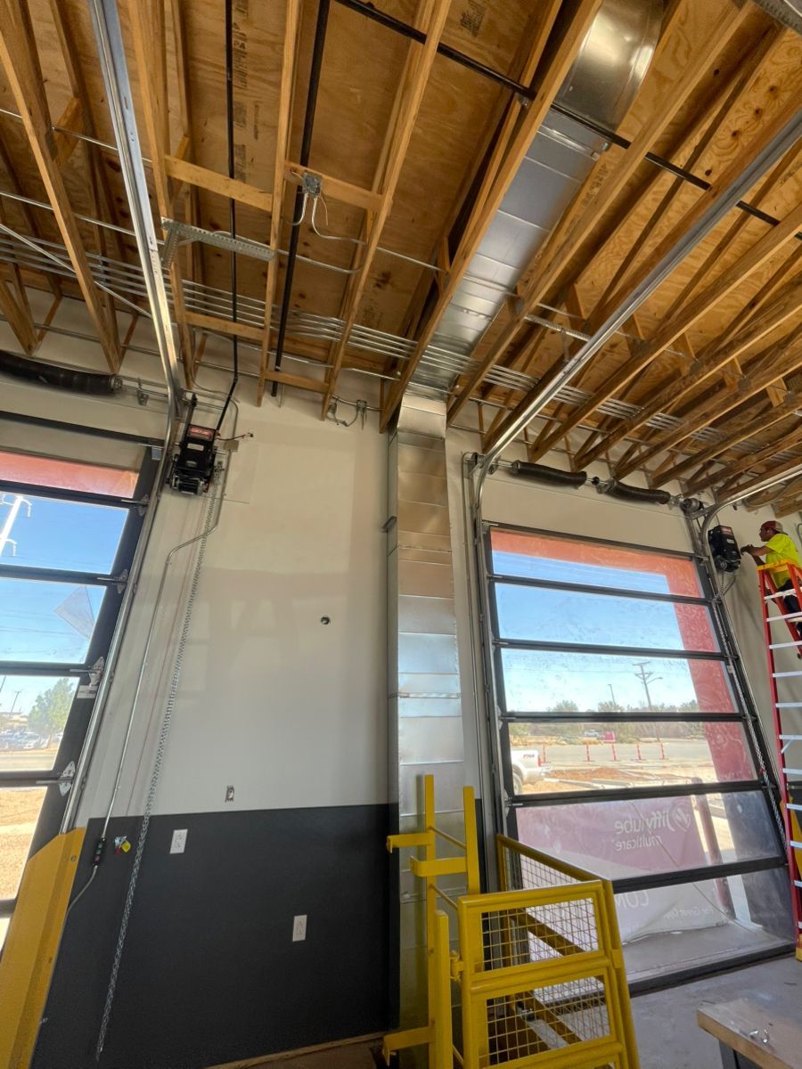 Interior construction scene with open glass garage doors, metal ductwork, and exposed wooden beams.