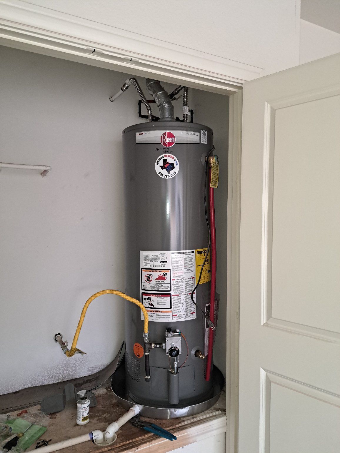 A tall, gray water heater sits in a closet. Plumbing connections are visible.