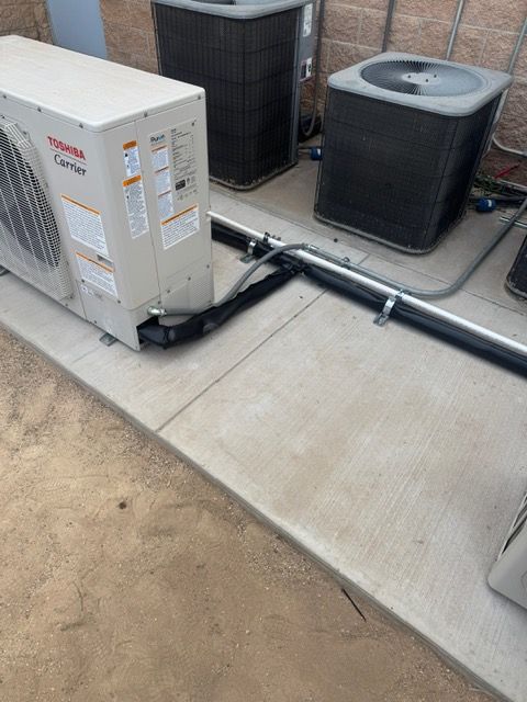 Outdoor HVAC units on a concrete pad. Gray and black. Piping visible.