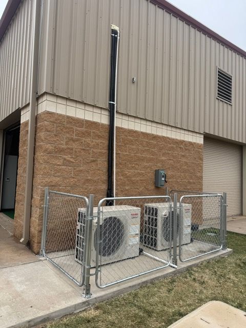 Air conditioning units outside a building, fenced in, with an exhaust pipe.