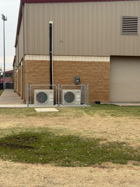 Two air conditioning units outside a building with a brick facade and a metal roof.