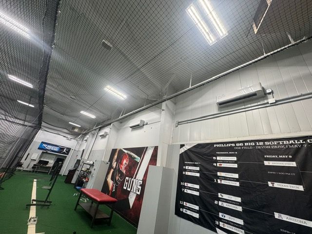 Indoor baseball/softball training facility with nets, banner, and turf flooring.