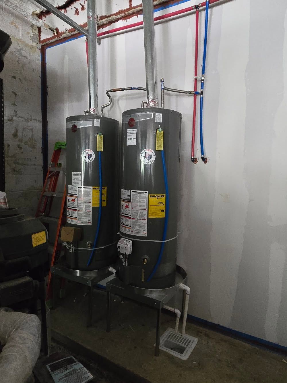 Two vertical gray water heaters side by side, pipes connected, in a utility room.