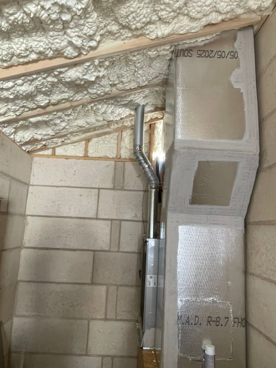 A metal chimney pipe runs up through a partially constructed wall with insulation and exposed cinder blocks.