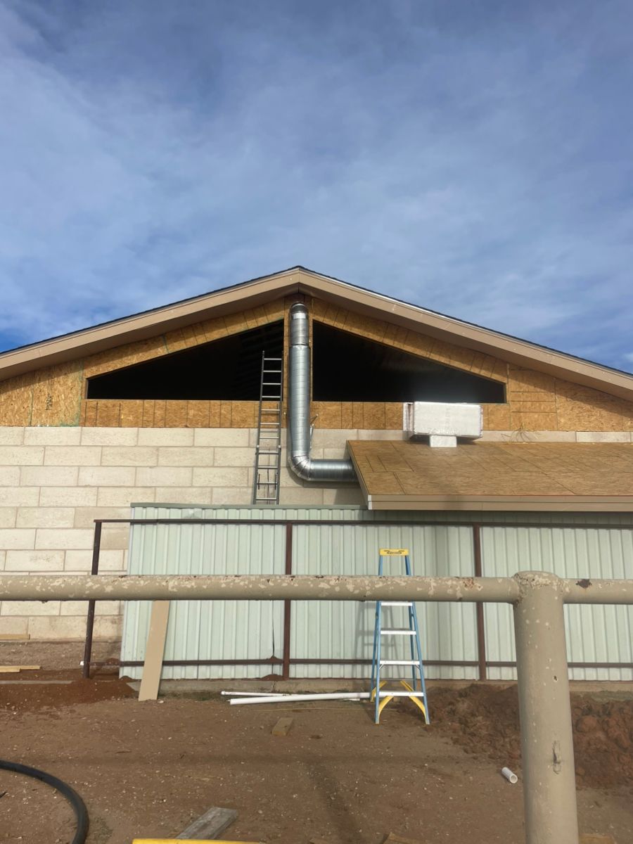 Building exterior with chimney pipe extending from the roof, a ladder, and a partly cloudy sky.